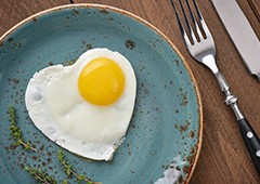 Fried egg in shape of heart on blue plate top view