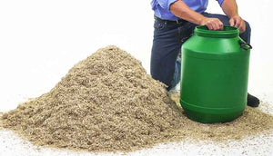 man with hand on green storage drum near pile of hemp bedding